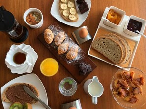 A breakfast table with croissants, bread, jam, butter, and a coffee pot.