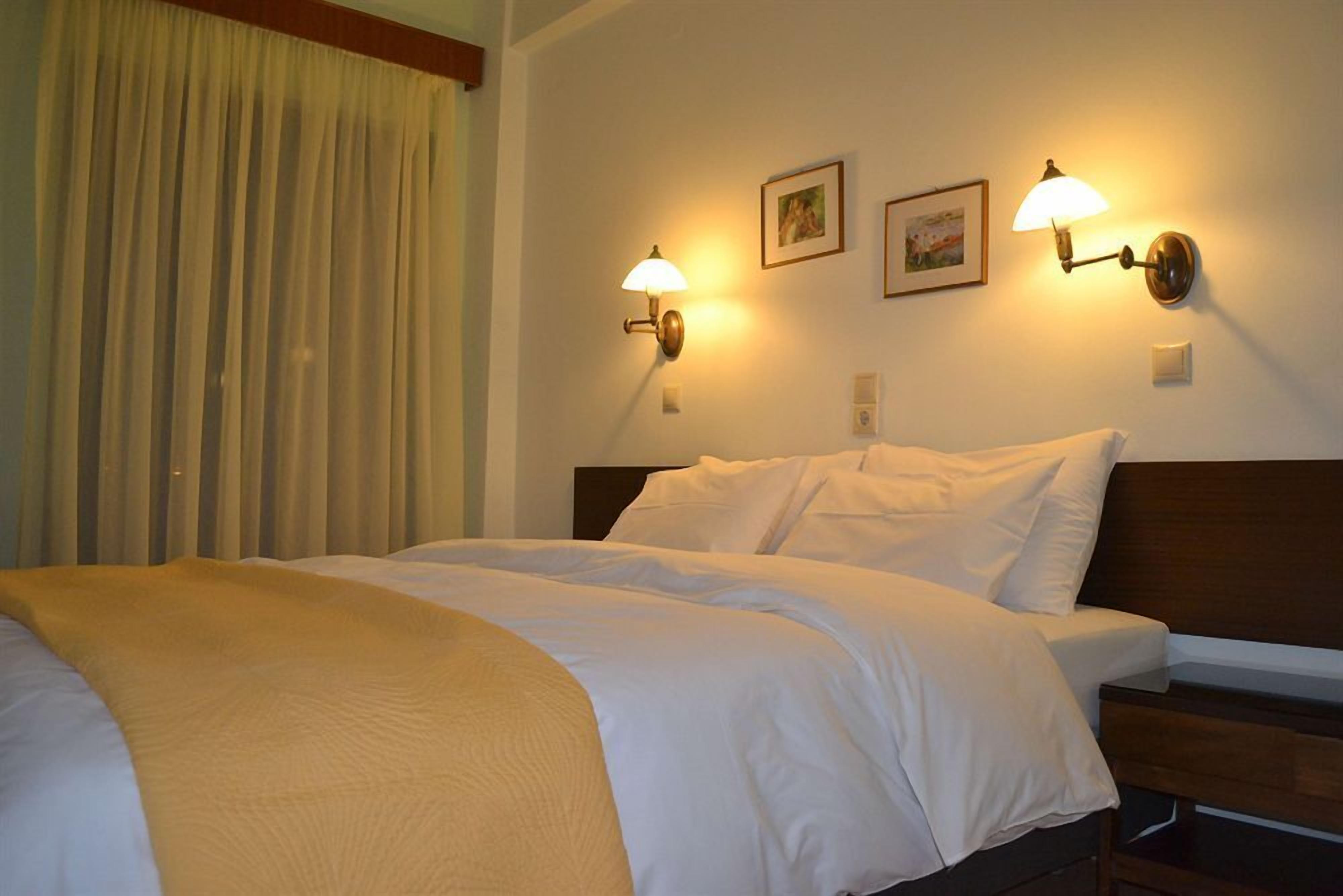 A hotel room with a bed, two wall-mounted lamps, and two framed pictures on the wall.
