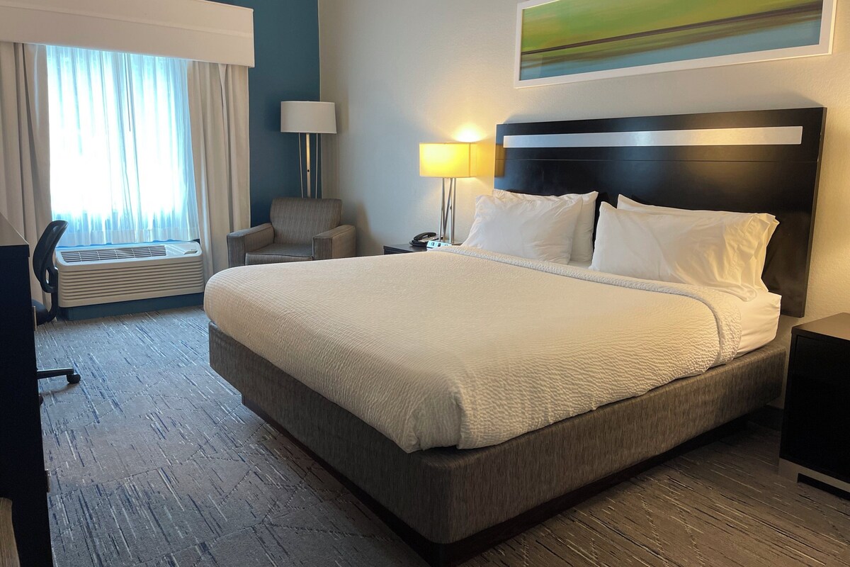 Een hotelkamer met een groot bed, een stoel, een bureau, een lamp en een schilderij aan de muur.