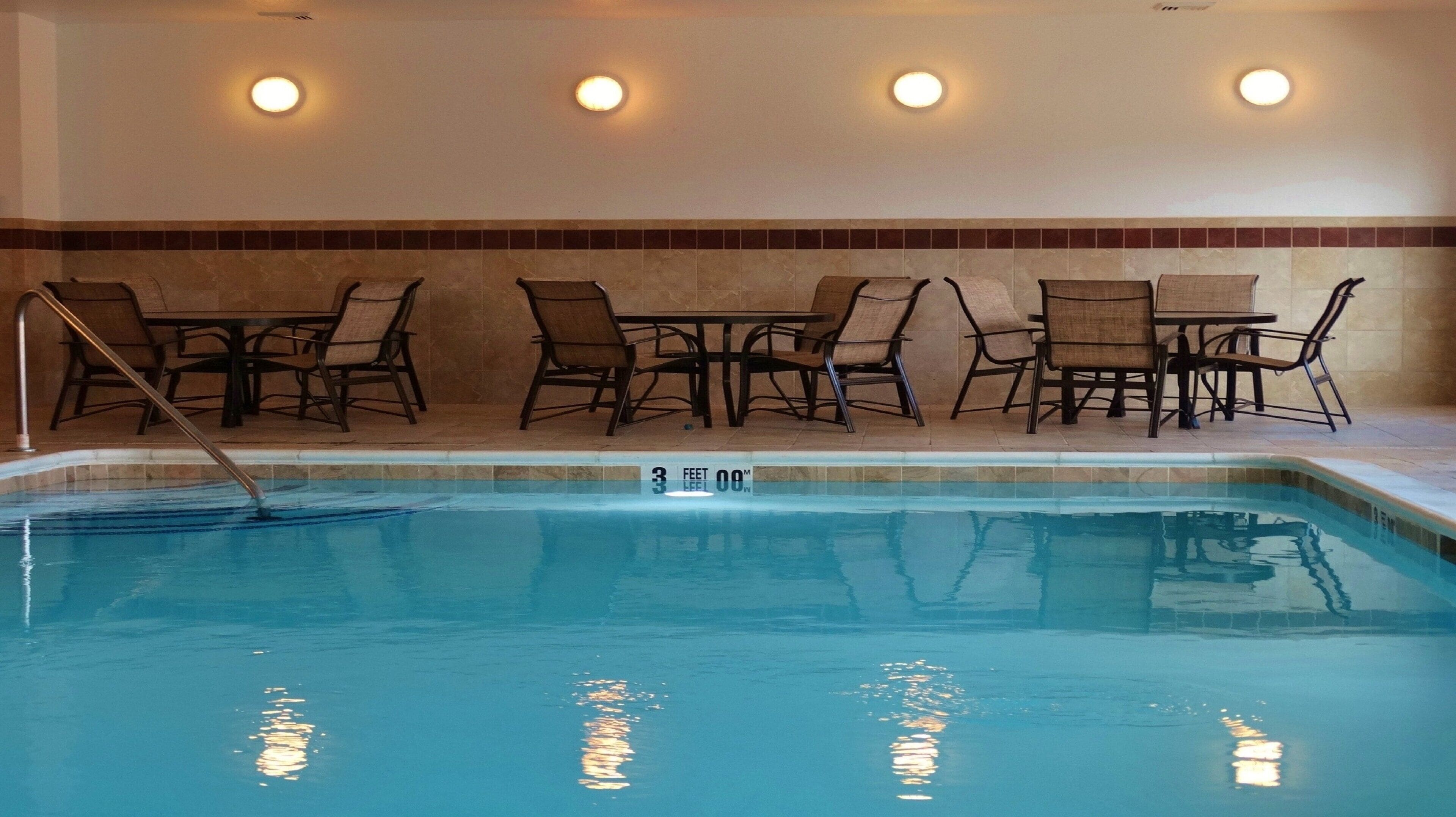 A swimming pool with a depth marker, surrounded by lounge chairs and tables, and recessed wall lighting.