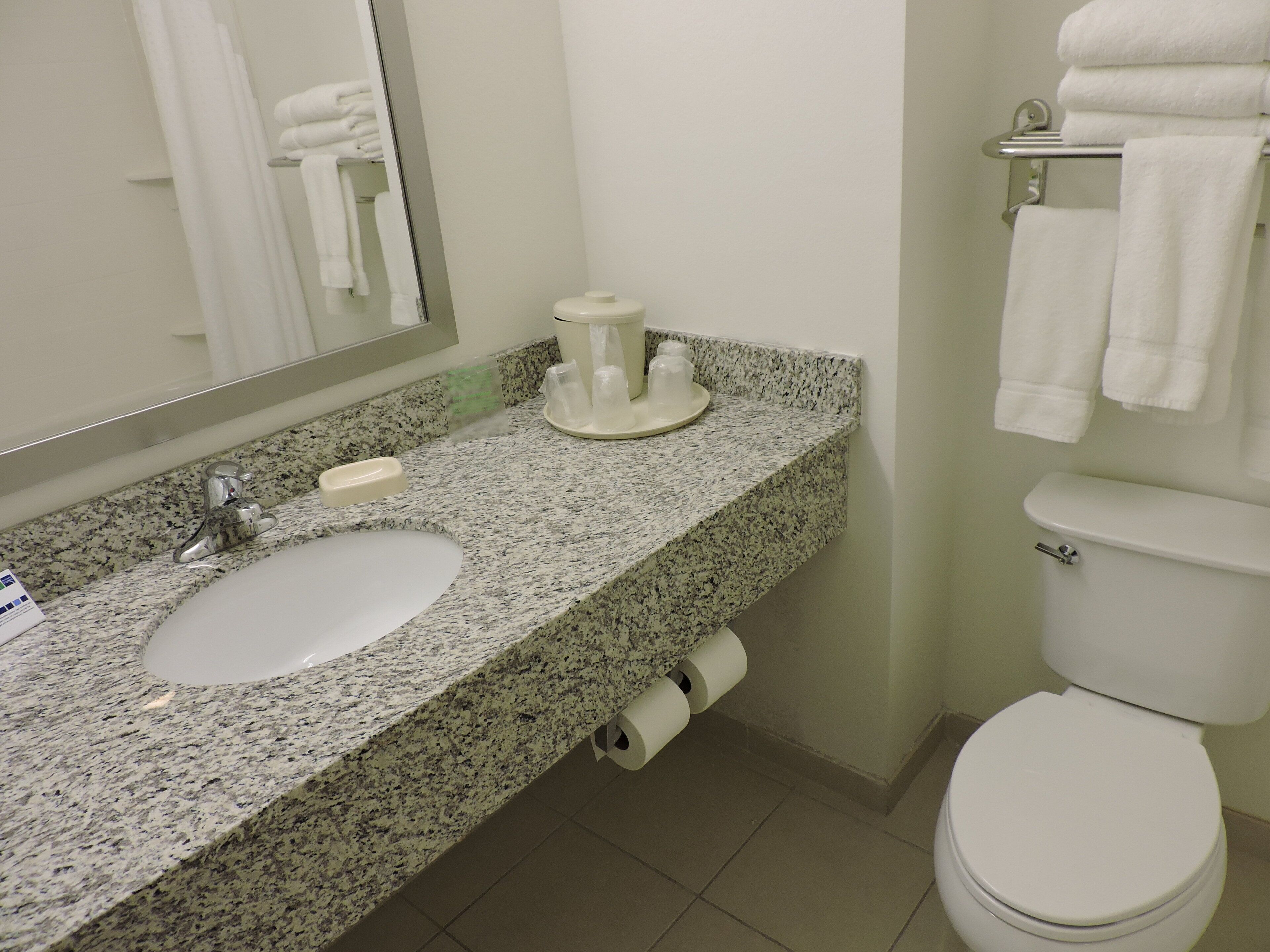 A bathroom with a granite countertop, a white sink, a toilet, and a towel rack.