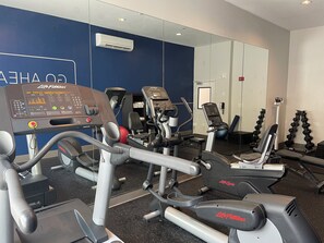 Een sportschool met diverse fitnessapparaten, waaronder loopbanden, een bankdrukpers en gewichtsschijven.