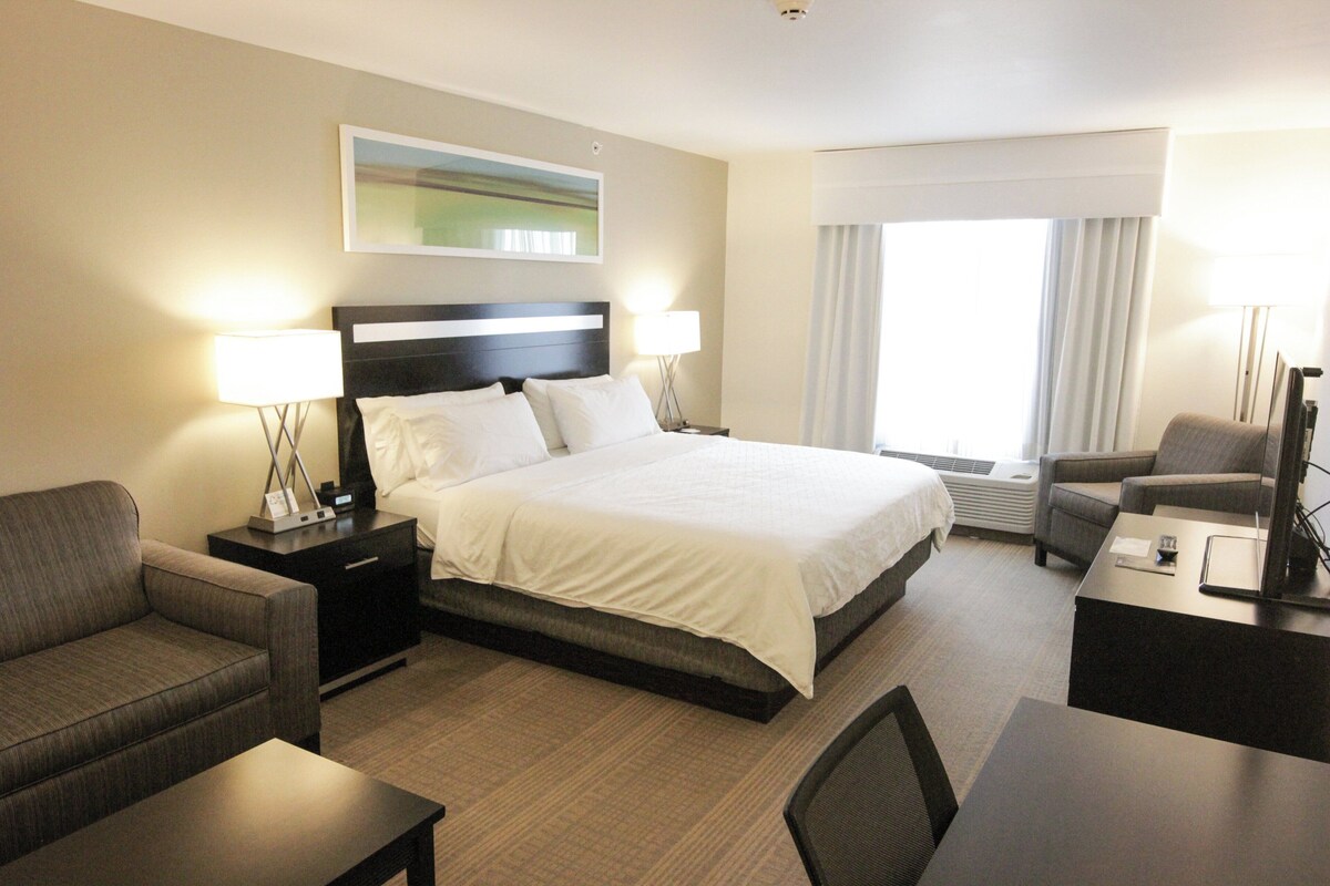 Een hotelkamer met een bed, twee nachtkastjes, een bureau, een stoel, een bank en een raam met gordijnen.