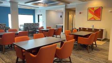 A modern dining area with orange chairs and dark tables, featuring a blue accent wall and a colorful abstract painting.