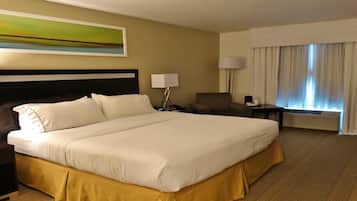 A hotel room with a large bed, a chair, a desk, a lamp, and a window with curtains.