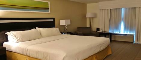 A hotel room with a large bed, a chair, a desk, a lamp, and a window with curtains.