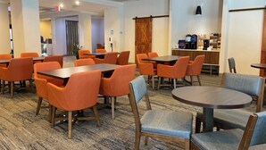 Un comedor de hotel con sillas y mesas naranjas, una estación de café y una puerta de madera.