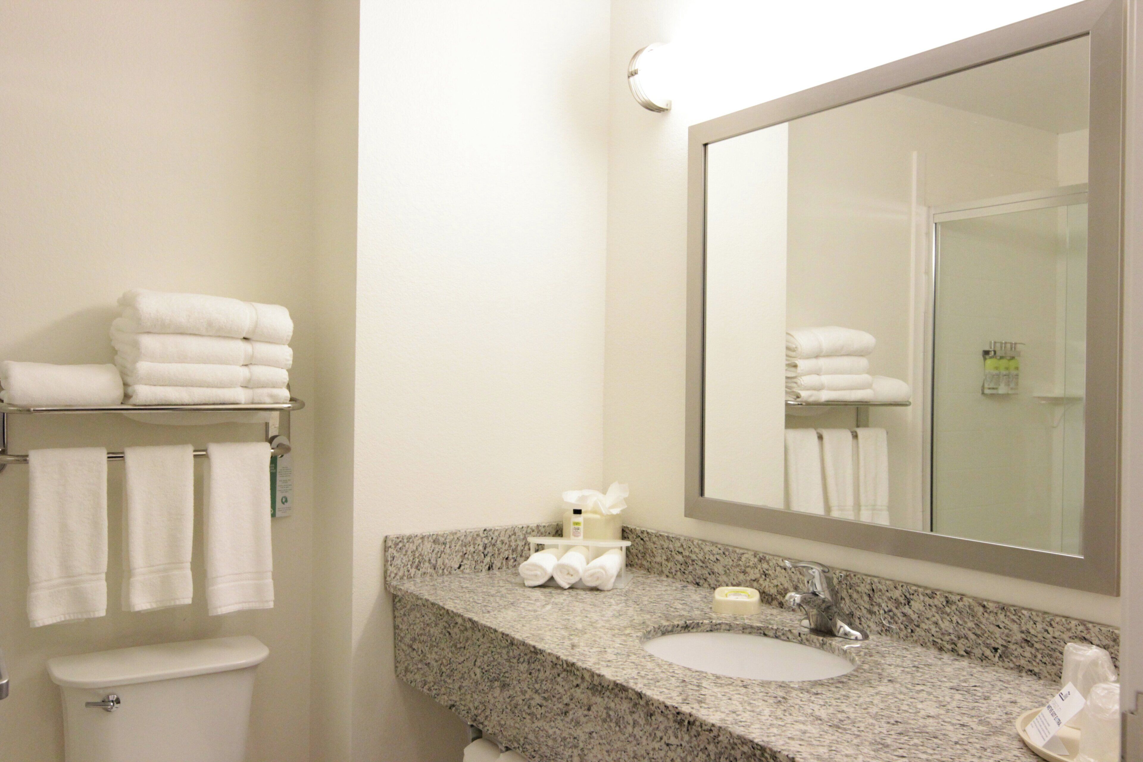 A bathroom with a granite countertop, a sink, a mirror, and a stack of white towels.