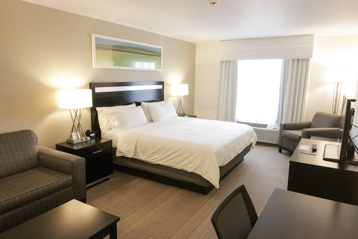 A hotel room with a large bed, two bedside tables with lamps, a sofa, a desk, and a chair.