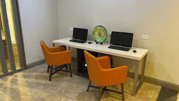 A workspace with two laptops on a white desk, two orange chairs, and a decorative glass object.