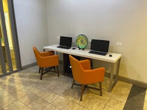 Een werkplek met twee laptops op een wit bureau, twee oranje stoelen en een decoratief glazen object.