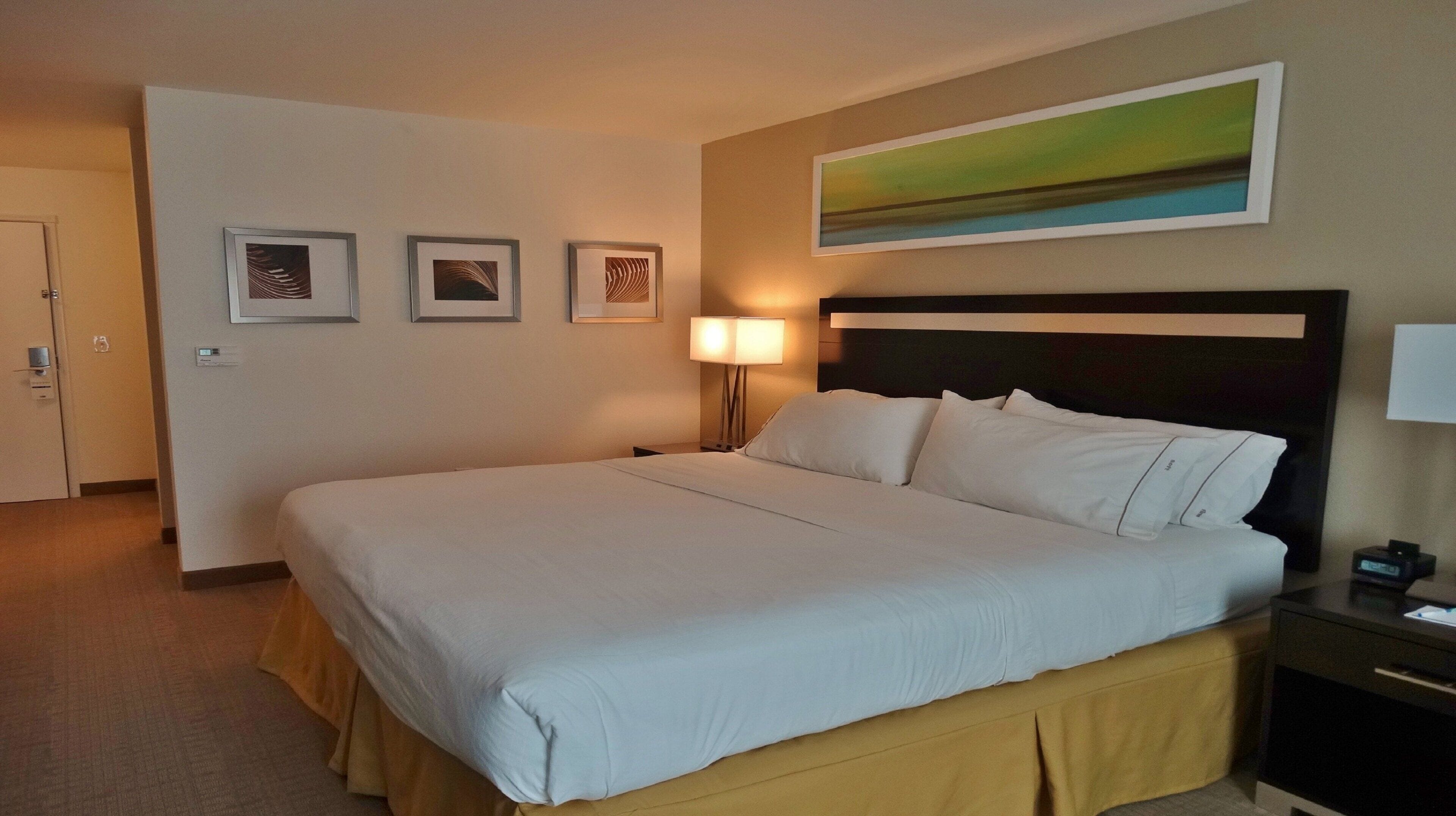 Ein Hotelzimmer mit einem großen Bett, einem Nachttisch mit Lampe und drei gerahmten Bildern an der Wand.