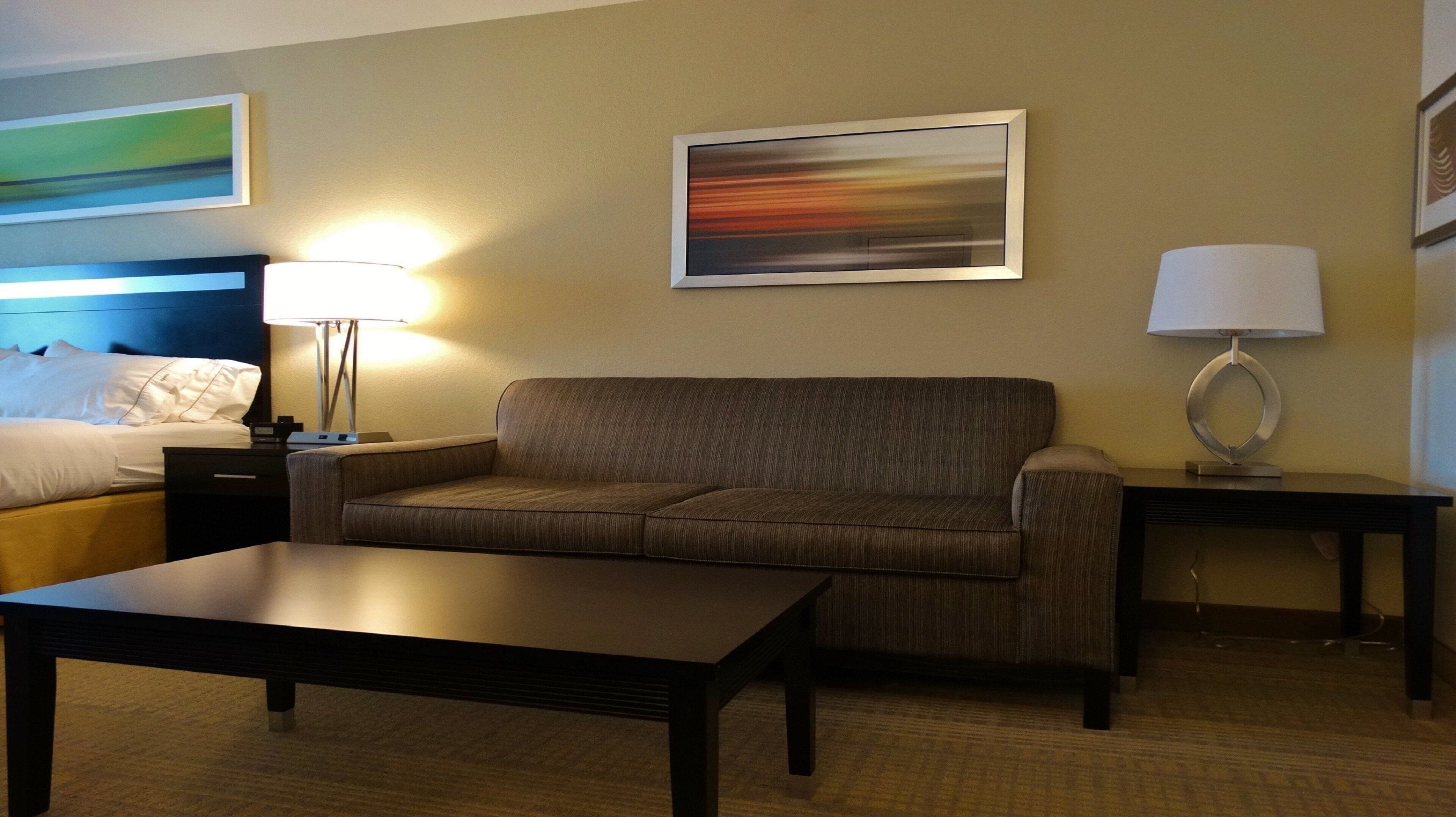 Una habitación de hotel con cama, sofá, mesa y dos lámparas.