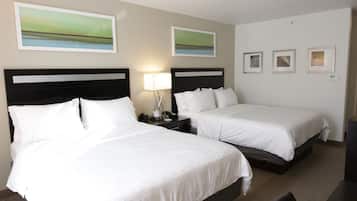 Habitación de hotel con dos camas, una mesita de noche con lámpara y tres cuadros enmarcados en la pared.