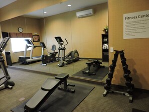 A fitness center with treadmills, elliptical machines, a bench, and dumbbells.