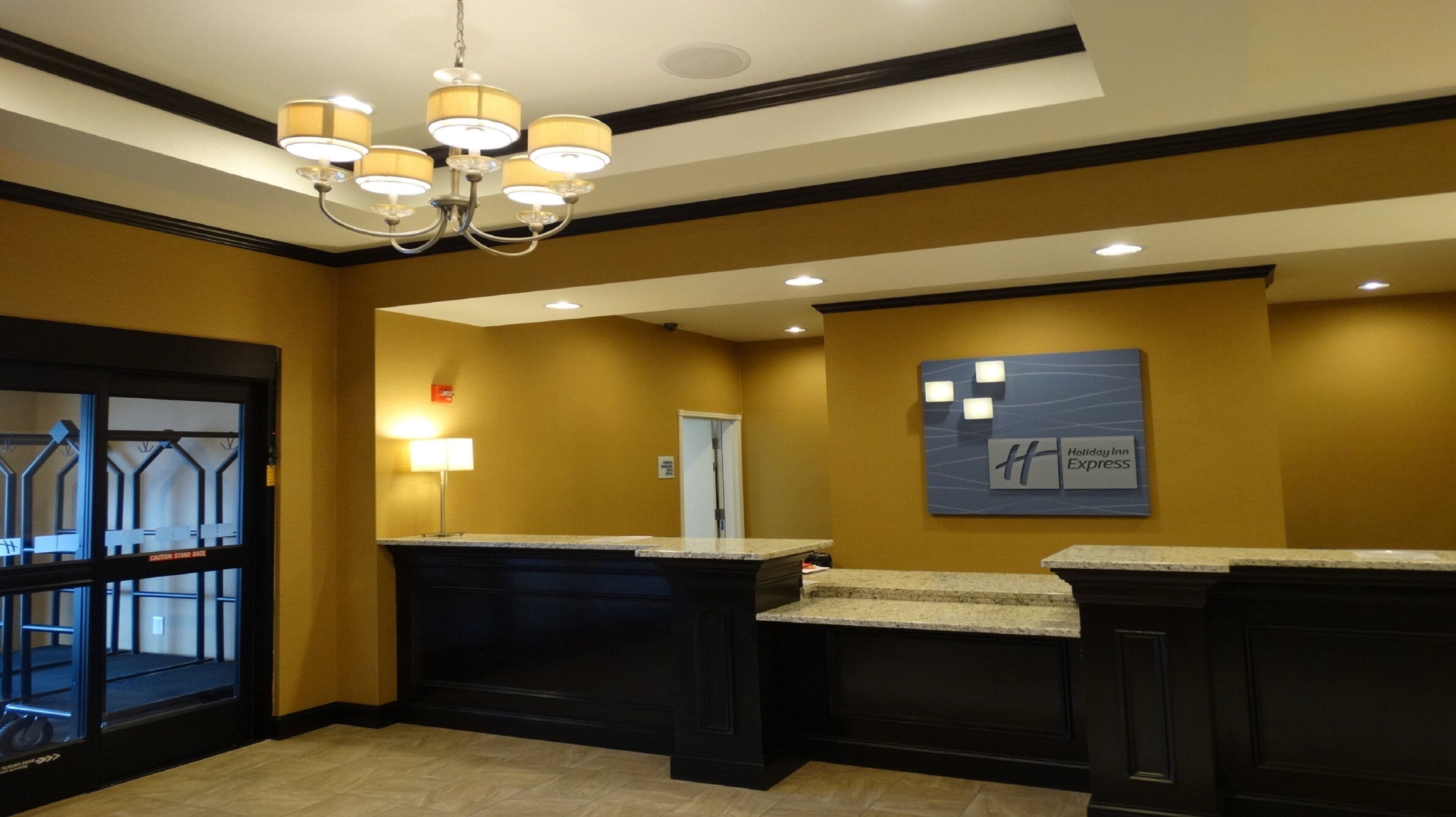 A hotel lobby with a reception desk, a chandelier, a wall-mounted sign, and a door.