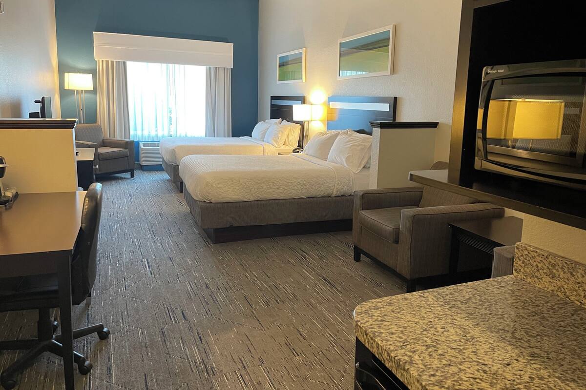A hotel room with two beds, a desk, a chair, a TV, and a window with curtains.