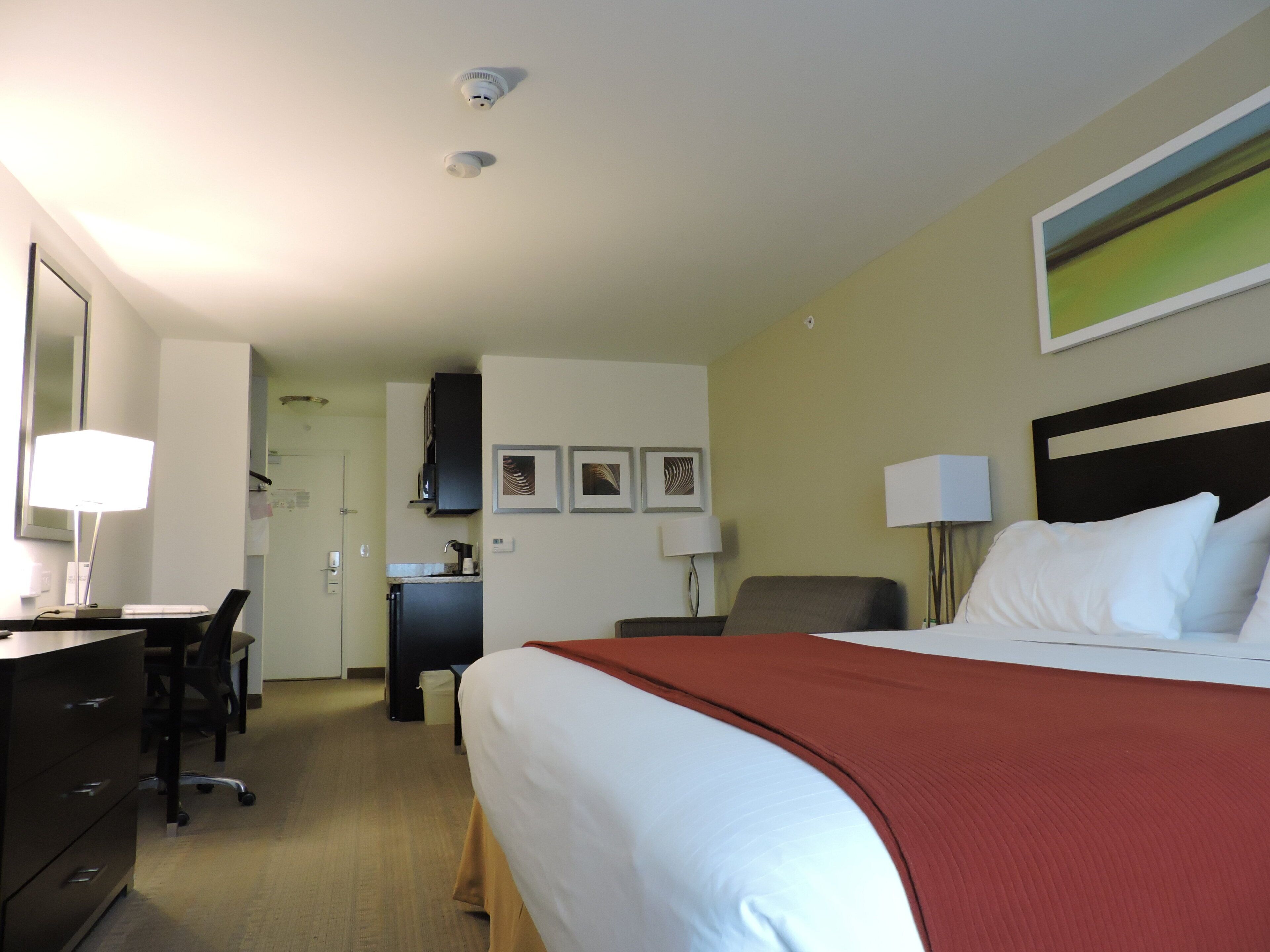 A hotel room with a bed, desk, chair, and a view of the hallway.