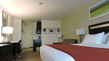 A hotel room with a bed, desk, chair, and a view of the hallway.