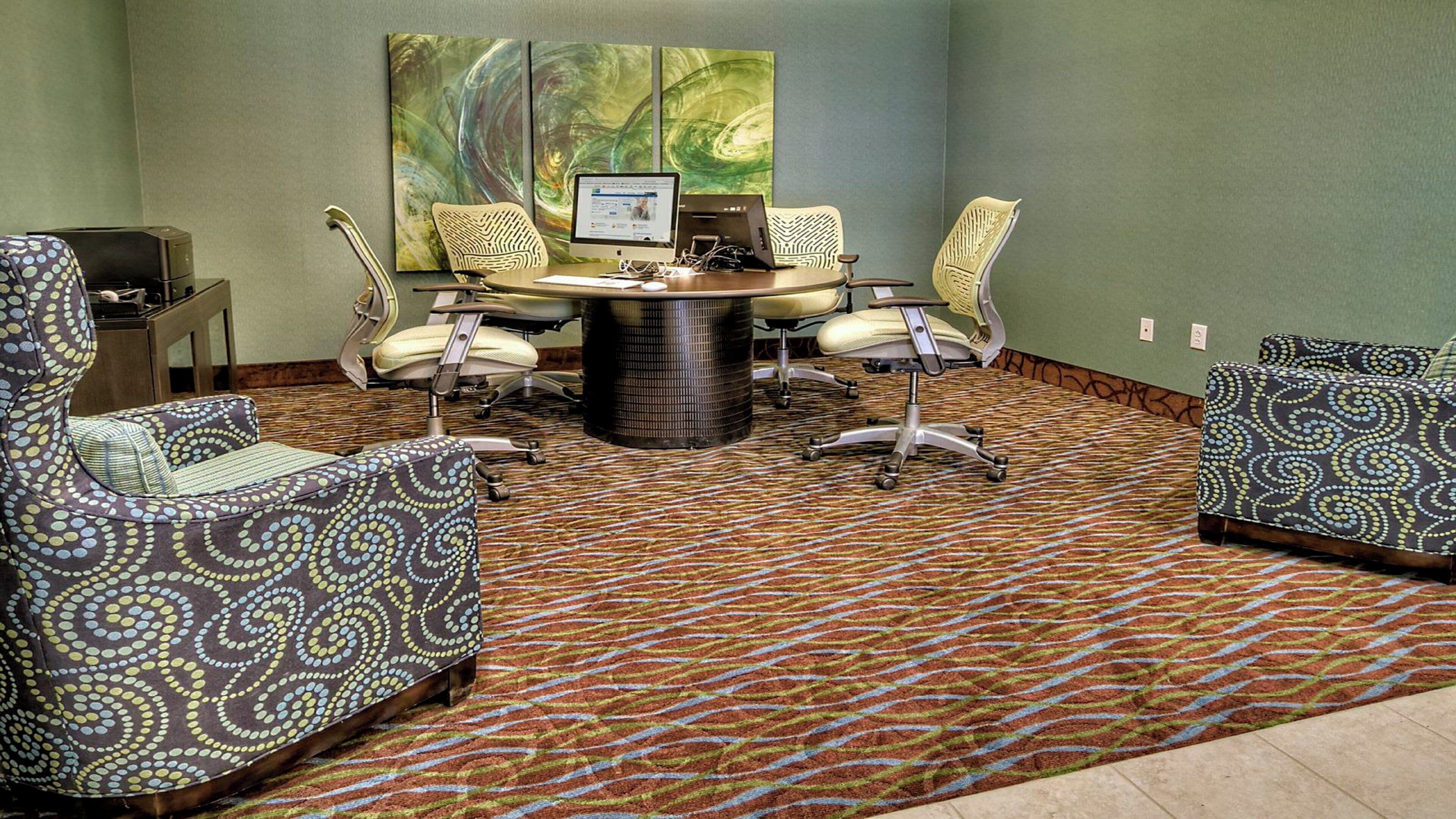 A conference room with a round table, four chairs, and a computer monitor.