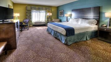 A hotel room with a large bed, a desk with a computer, a chair, and a TV.