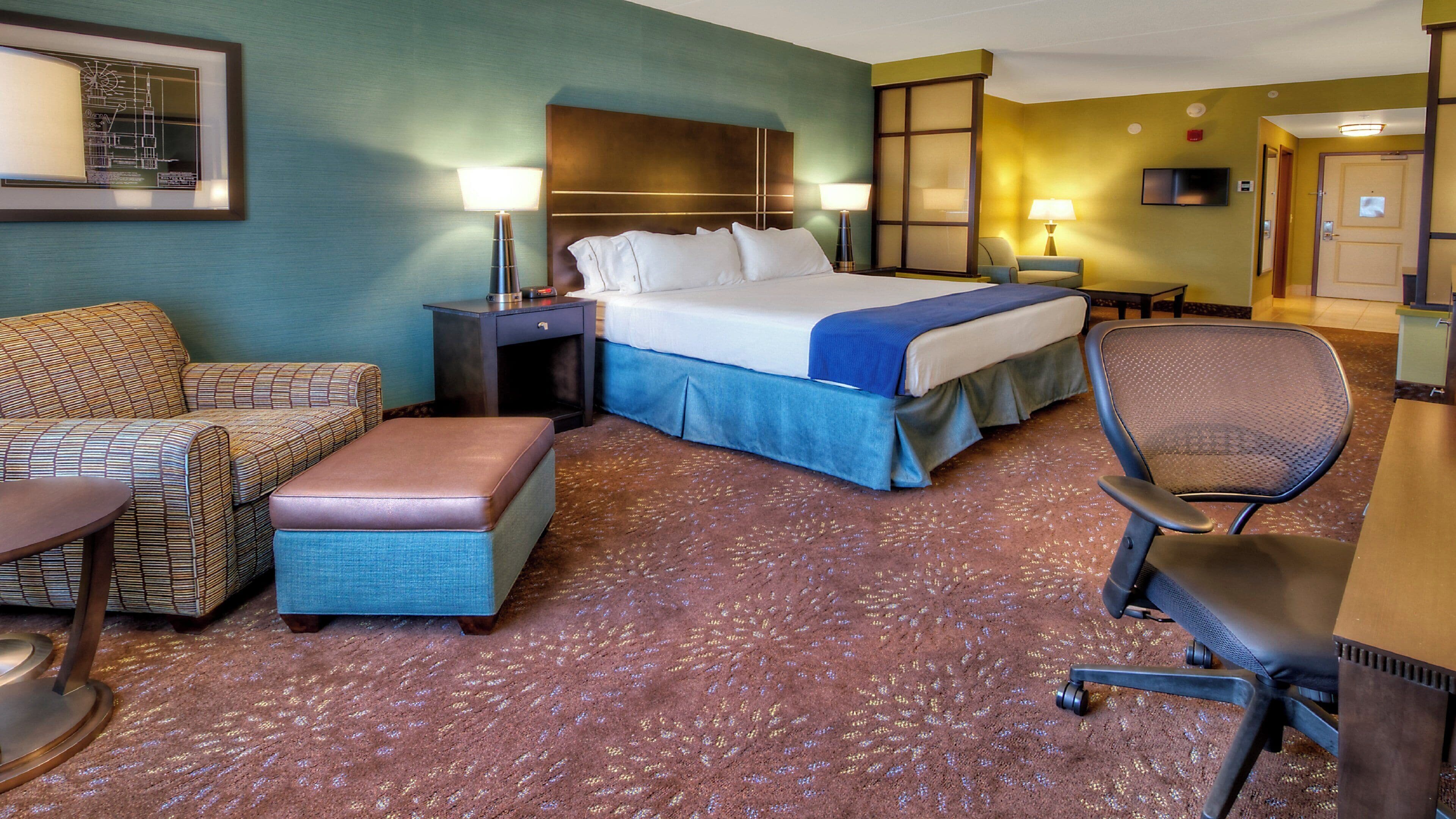 A hotel room with a bed, a desk, a chair, a sofa, and a small table.