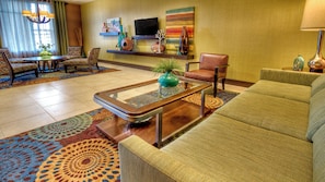 A hotel lobby with a sofa, chairs, a coffee table, a TV, and decorative items on shelves.
