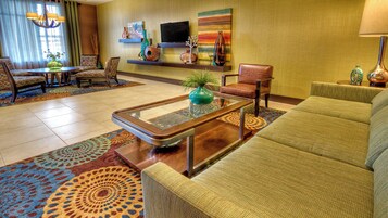 Un hall de hotel con un sofá, sillas, una mesa de centro, un televisor y objetos decorativos en estantes.