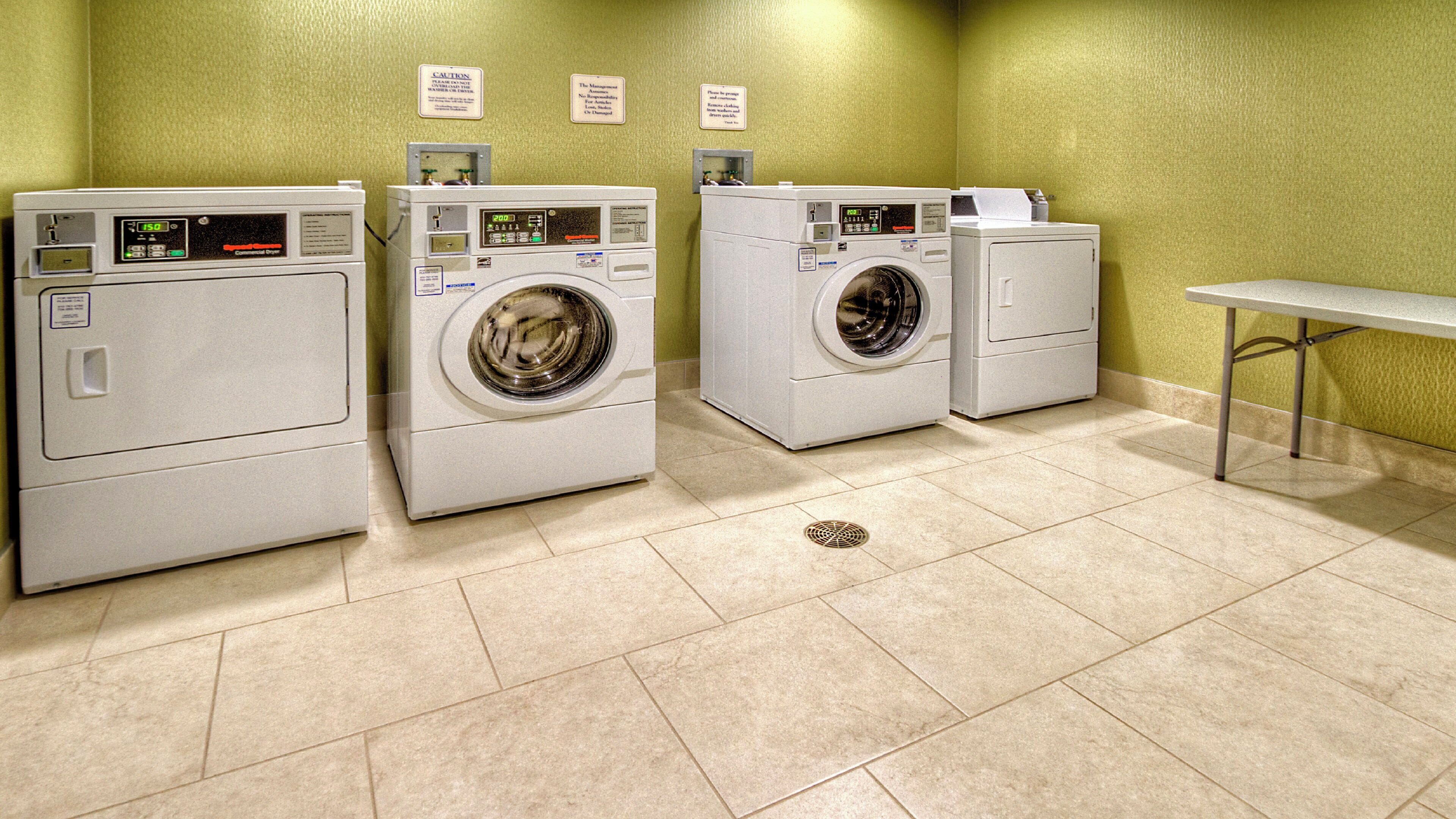 A laundry facility with three washing machines and a table.