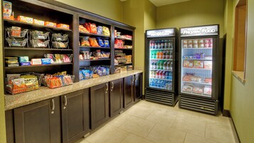 Un área de comida autoservicio con dispensadores de bebidas refrigeradas y estantes llenos de aperitivos y bebidas.