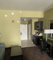 Habitación de hotel con kitchenette, un pequeño comedor y una puerta que da a otra habitación.
