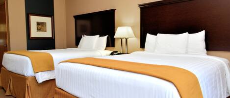 A hotel room with two beds, each with white linens and a brown throw blanket. There is a bedside table with a lamp and a phone.