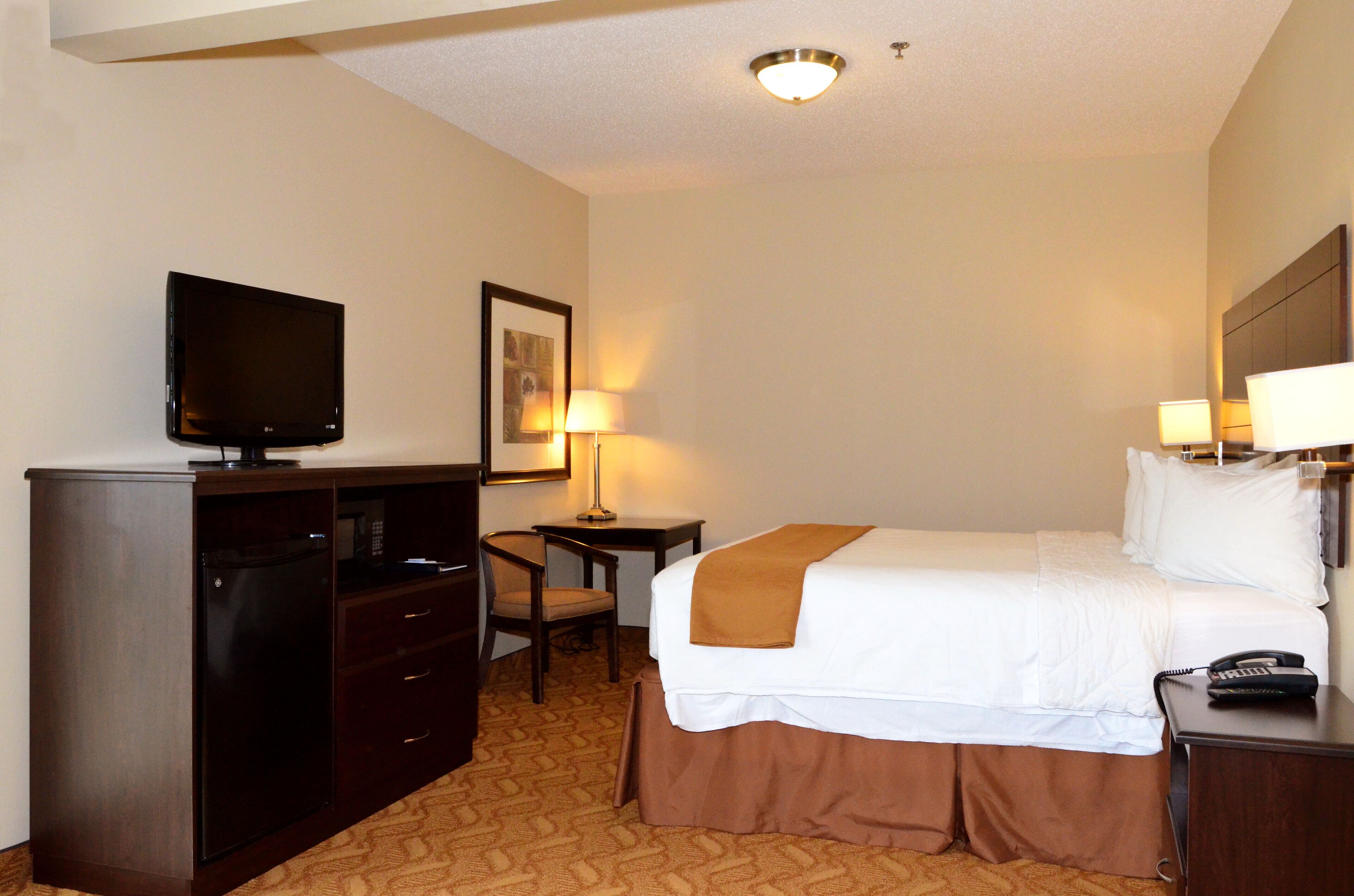 A hotel room with a bed, a desk, a chair, a television, and a telephone.