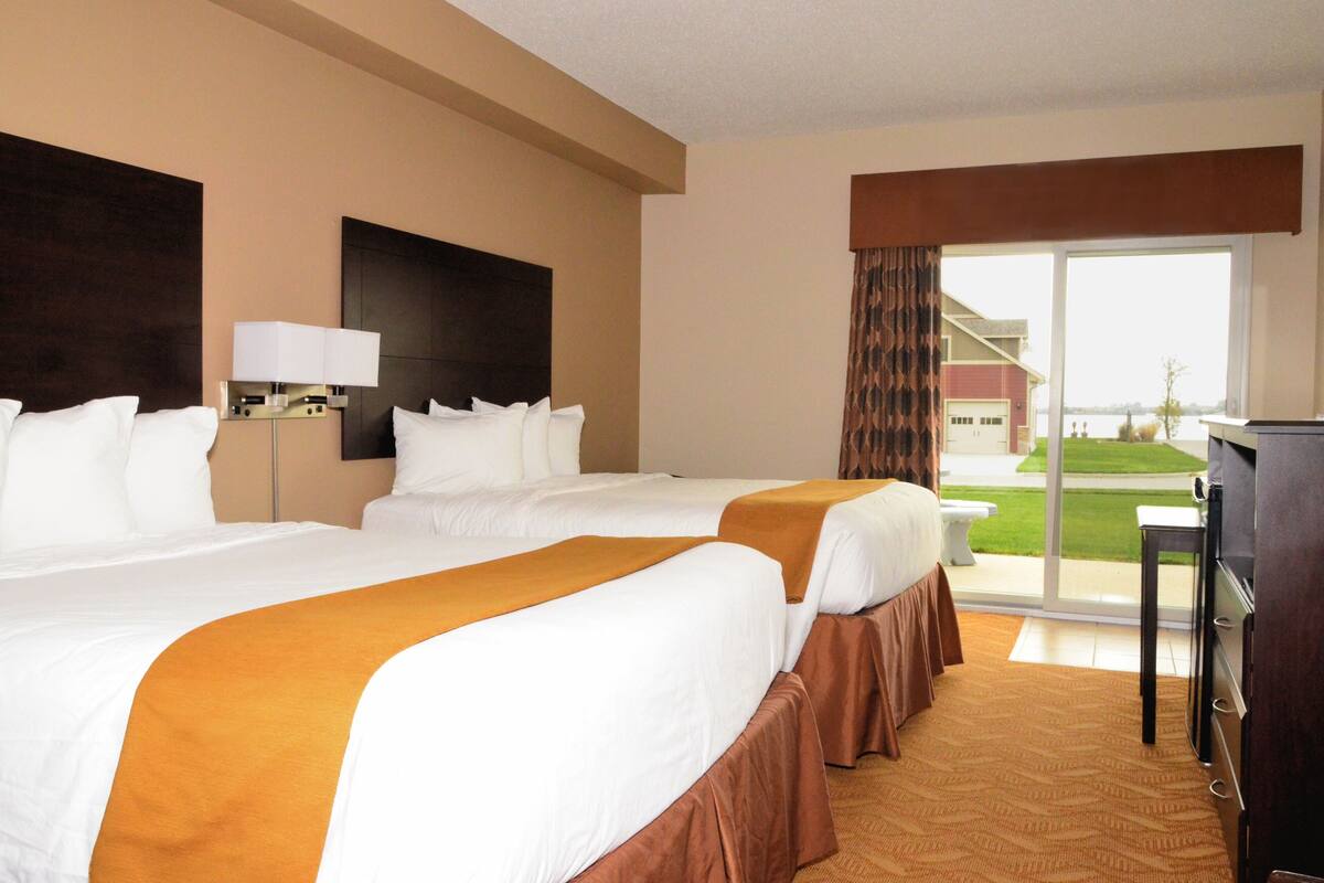 A hotel room with two beds, a desk, and a large window offering a view of the outdoors.
