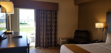 A hotel room with a bed, a desk with a lamp, a chair, a window with curtains, and a view of a golf course.