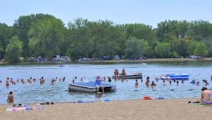 A beach with people swimming and boats on the water.