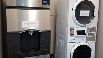 A compact kitchenette with a refrigerator, a water dispenser, and a stacked washer and dryer unit.