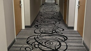 Un couloir d’hôtel avec un tapis à motifs, des portes numérotées 201 et 202, et un long couloir menant à une chambre.