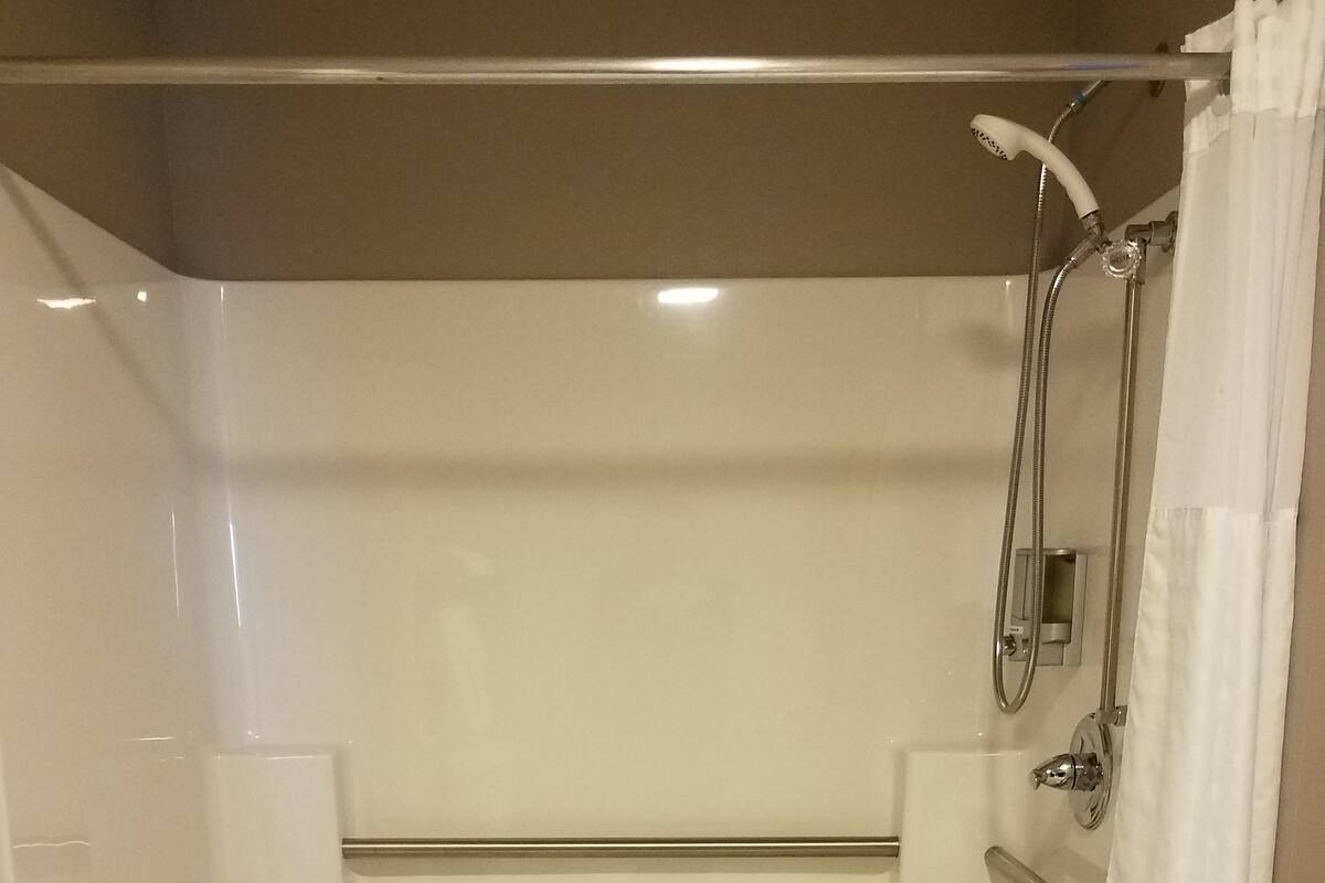 Ducha a ras de suelo con suelo de azulejos blancos, cabezal de ducha, ducha de mano y toallero con una toalla y una barra de jabón.