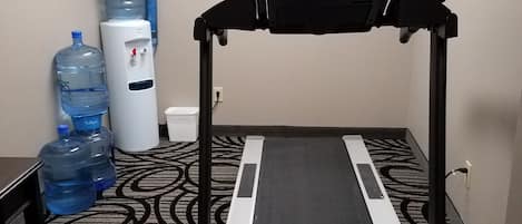 A hotel room with a treadmill, large water jugs, and a patterned carpet.