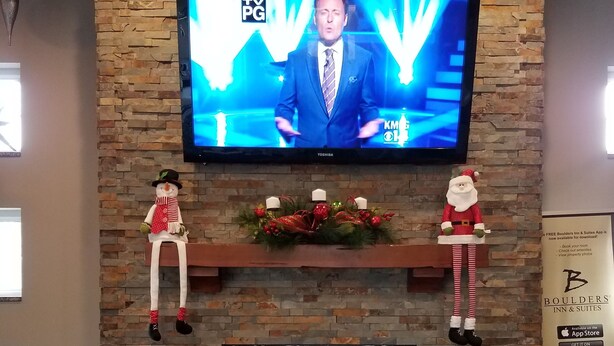 A TV mounted on a stone wall with a fireplace below. - Okoboji Inn & Suites (Milford)