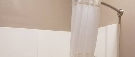 A white shower curtain in a bathroom with a bathtub.
