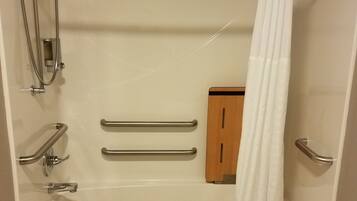 Un baño moderno con bañera, ducha, barras de apoyo y un armario de madera.