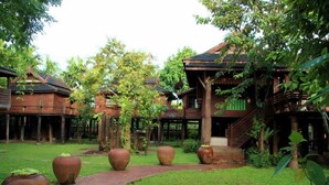 A traditional wooden building with a covered walkway and large clay pots in the garden. - Lanna Ricebarn (Chiang Mai)