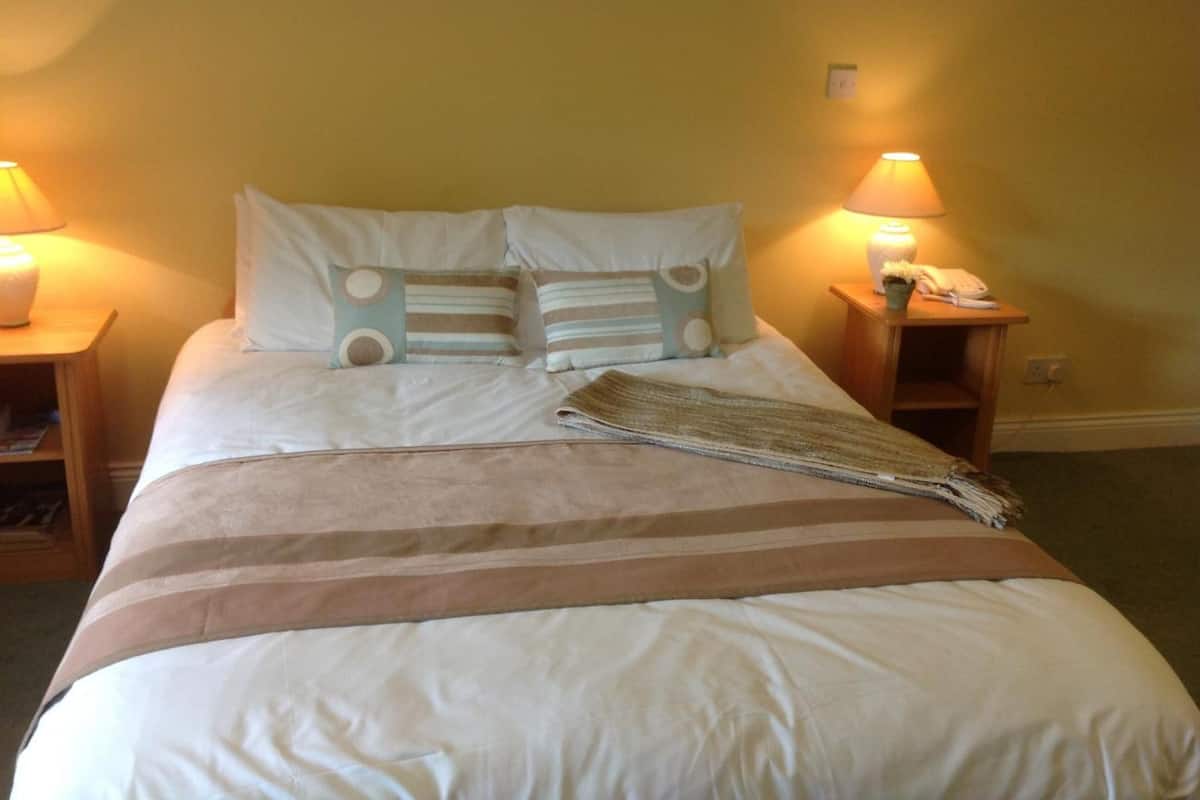 A neatly made bed with pillows and a blanket, two bedside lamps, and a telephone on a wooden nightstand.