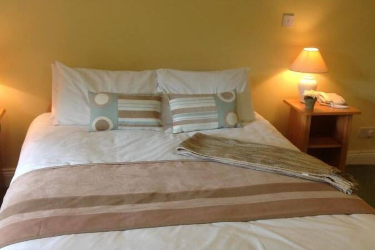 A bed with white and striped bedding, a lamp on a bedside table, and a folded blanket on the bed.
