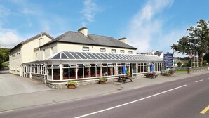 A building with a covered patio area, a signboard, and a flag. - Abbey Hotel (Ballyvourney)