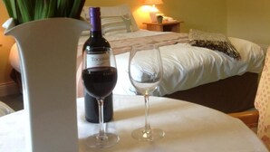 A hotel room with a bed, a bedside table with a lamp, a vase with flowers, and two wine glasses. - Abbey Hotel (Ballyvourney)