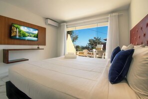 A hotel room with a large bed, a television mounted on the wall, a balcony with a table and chairs, and a view of the outdoors.