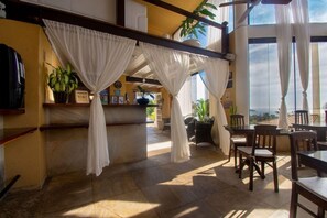 A room with a bar area, seating, and large windows.